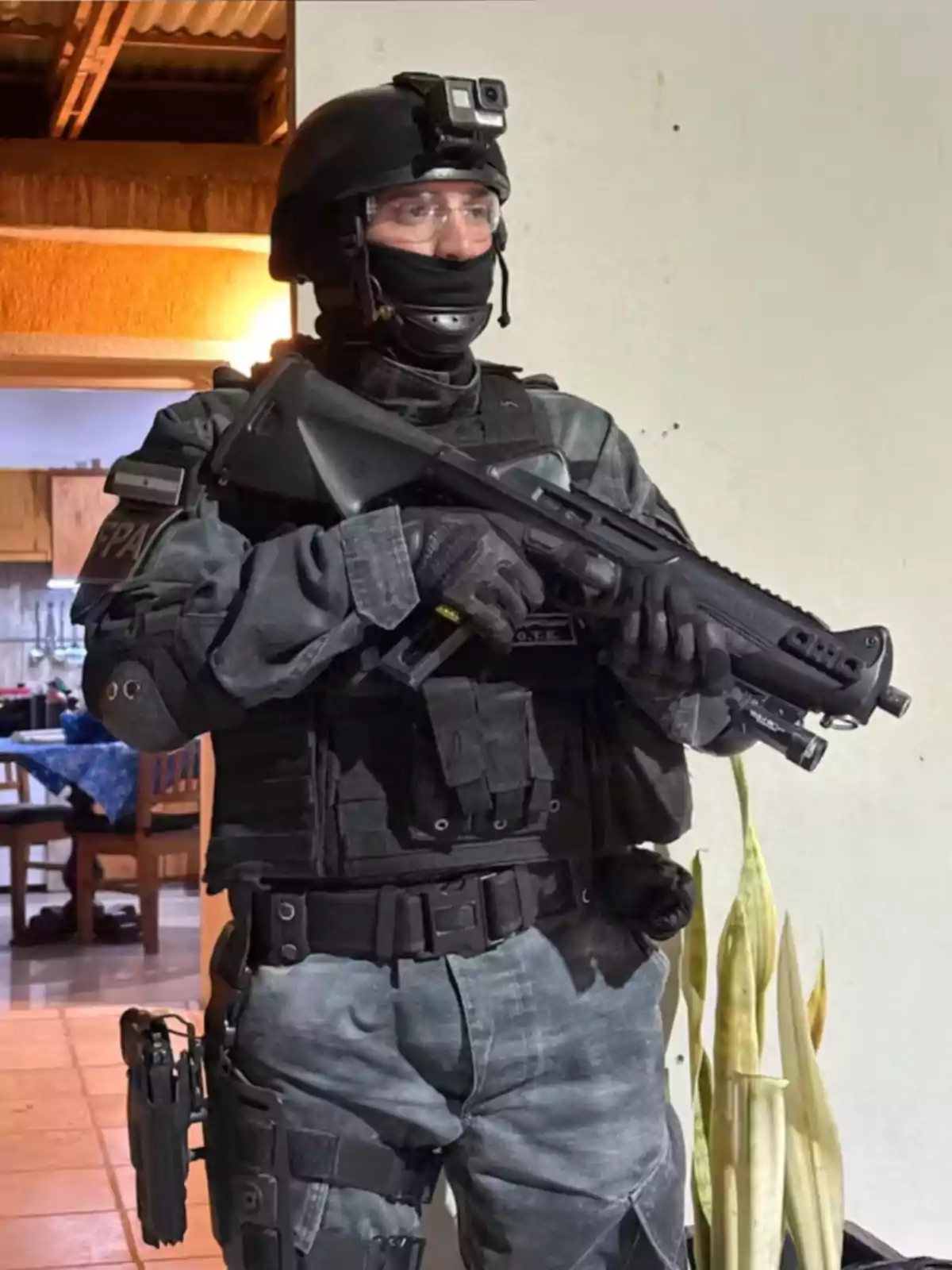 Un agente de policía fuertemente armado con uniforme táctico y casco sostiene un arma dentro de una casa Un agente de policía fuertemente armado con uniforme táctico y casco sostiene un arma dentro de una casa