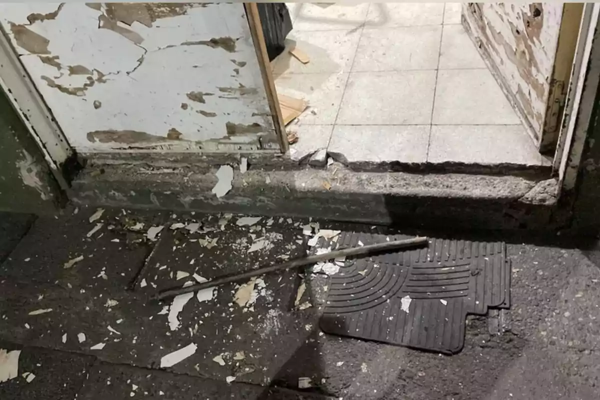 Damaged door with peeling paint, debris, and a metal bar on a black mat at the entrance Damaged door with peeling paint, debris, and a metal bar on a black mat at the entrance