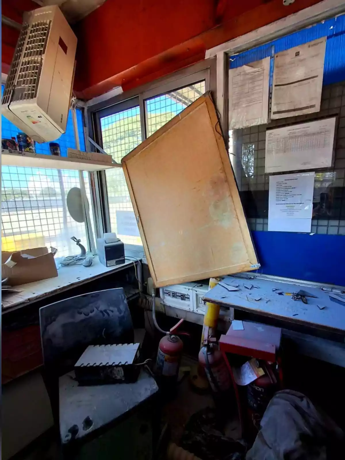Messy office with an air conditioner in the upper corner, a whiteboard fallen on the desk, papers stuck to the window, and fire extinguishers on the floor Messy office with an air conditioner in the upper corner, a whiteboard fallen on the desk, papers stuck to the window, and fire extinguishers on the floor