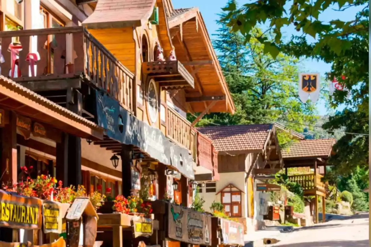 Calle de un pueblo con arquitectura de estilo alpino, casas de madera, flores en los balcones y árboles verdes bajo un cielo despejado Calle de un pueblo con arquitectura de estilo alpino, casas de madera, flores en los balcones y árboles verdes bajo un cielo despejado