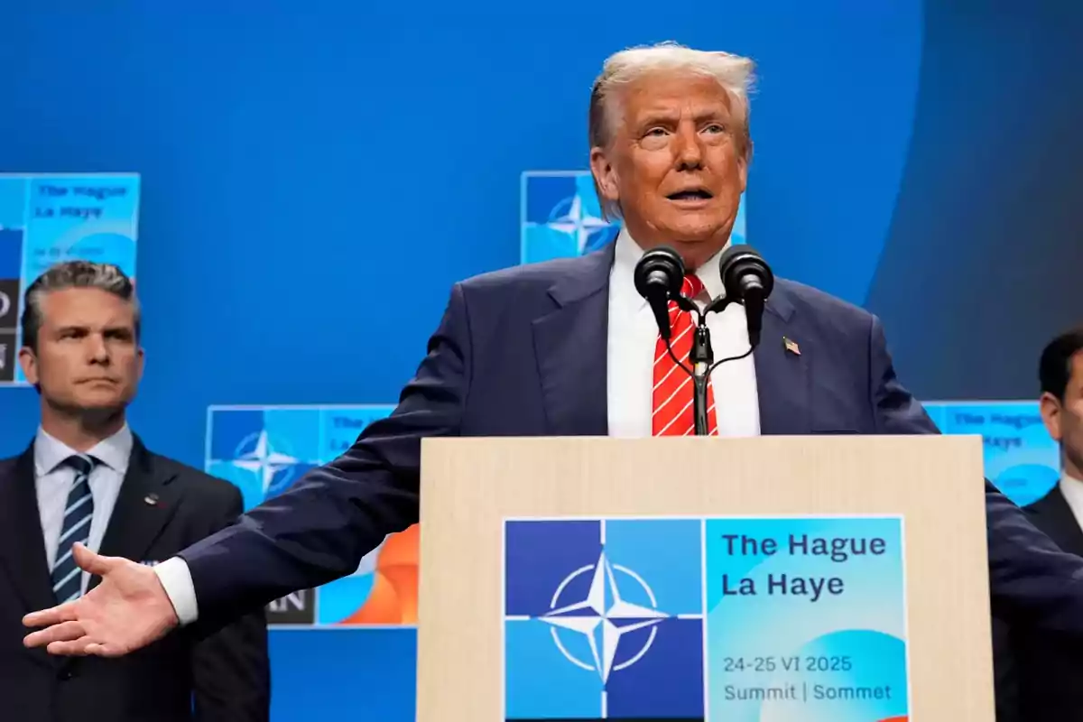 Blond-haired man in a blue suit and red tie speaking at a podium during a NATO summit in The Hague in 2025