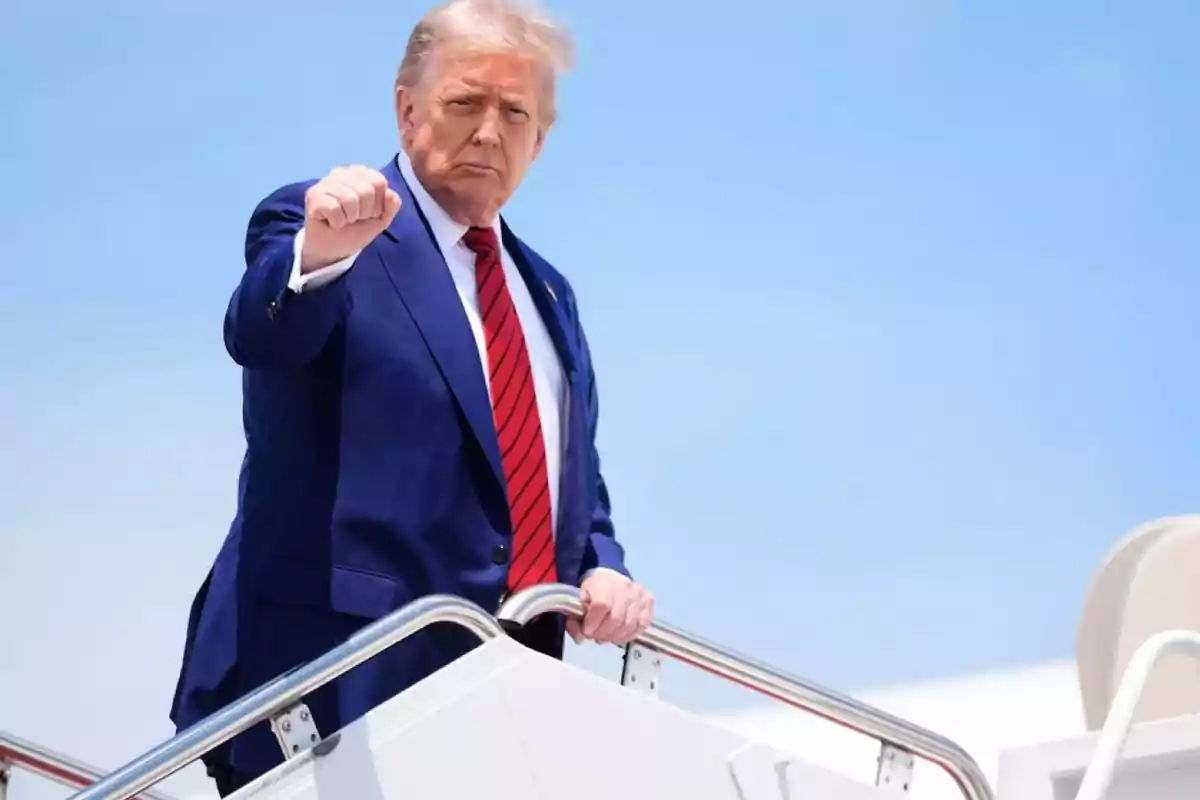 Hombre de traje azul y corbata roja subiendo las escaleras de un avión con el puño levantado bajo un cielo despejado Hombre de traje azul y corbata roja subiendo las escaleras de un avión con el puño levantado bajo un cielo despejado