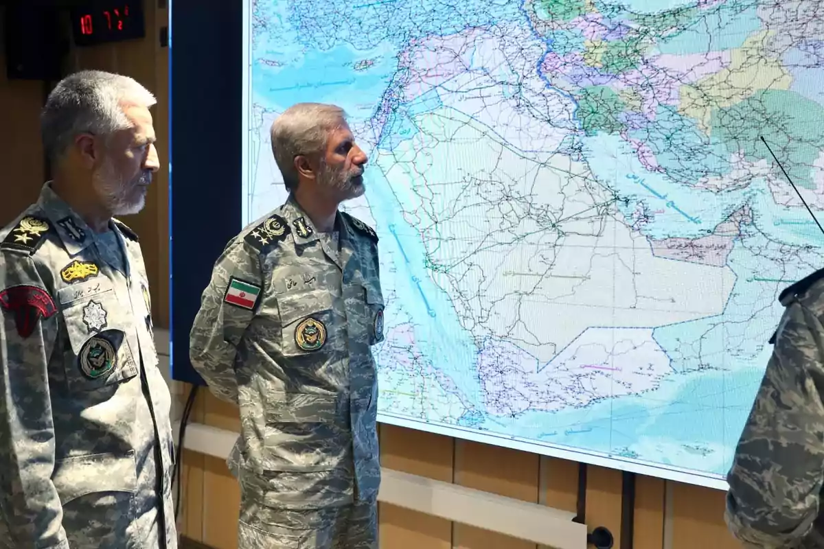 Military personnel in camouflage uniforms observe a large geographic map on a screen inside a command room. Military personnel in camouflage uniforms observe a large geographic map on a screen inside a command room.