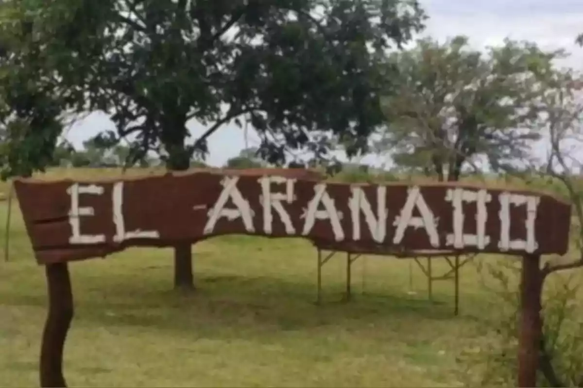 Wooden sign with the words EL ARANAIO in a field with trees in the background Wooden sign with the words EL ARANAIO in a field with trees in the background