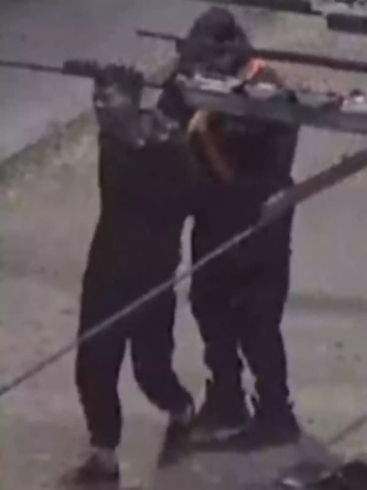 Dos personas vestidas de negro y encapuchadas portan armas largas mientras caminan por una calle durante la noche Dos personas vestidas de negro y encapuchadas portan armas largas mientras caminan por una calle durante la noche