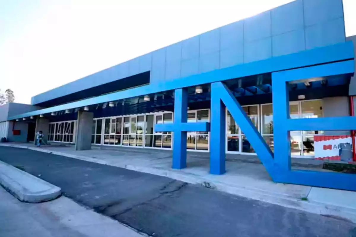 Fachada de un edificio moderno con grandes letras azules que forman la palabra TNE en la entrada Fachada de un edificio moderno con grandes letras azules que forman la palabra TNE en la entrada