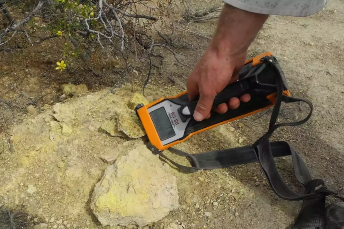 Persona usando un medidor portátil de radiación sobre una roca amarilla en un terreno árido