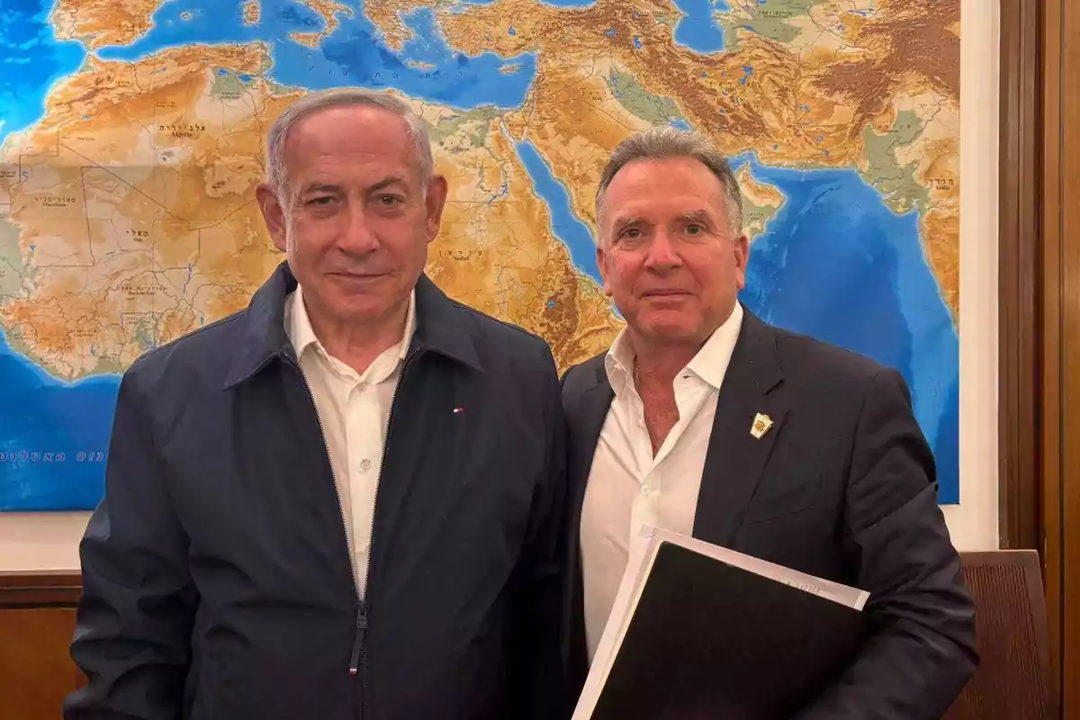 Two middle-aged men pose together in front of a large geographic map showing Europe, Africa, and the Middle East. Two middle-aged men pose together in front of a large geographic map showing Europe, Africa, and the Middle East.