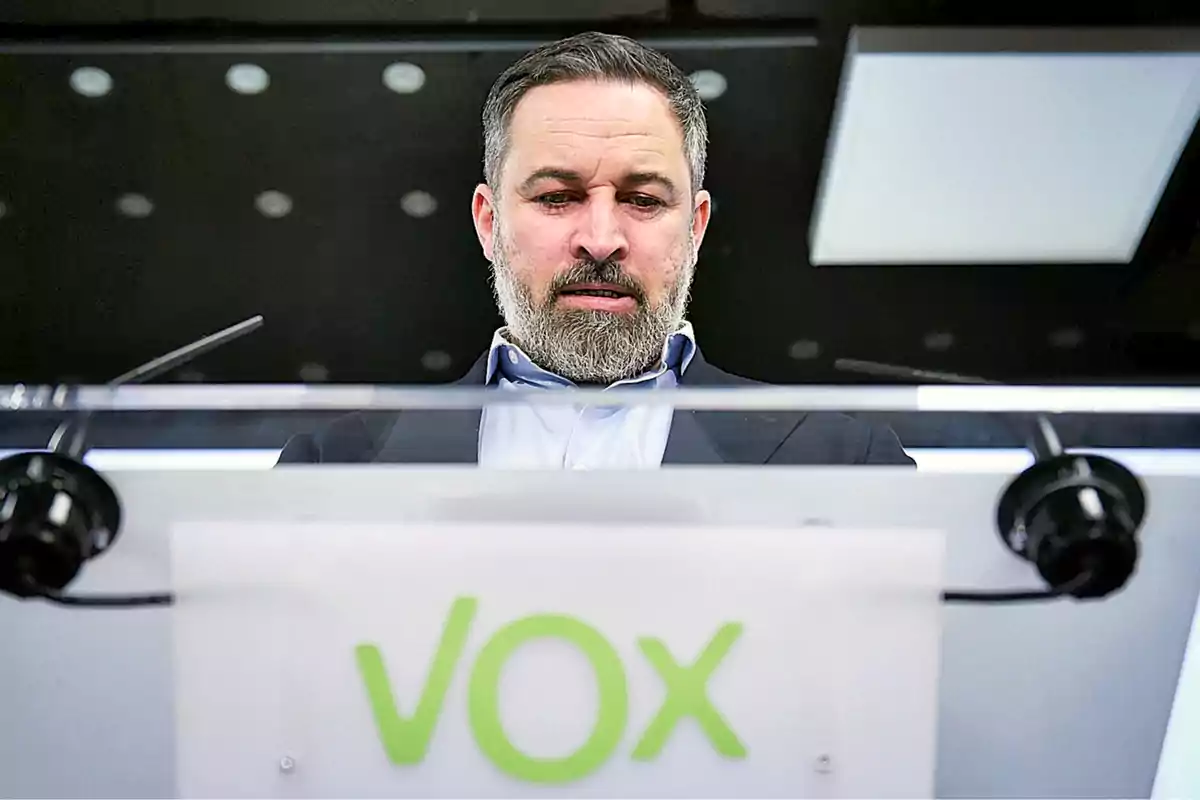Hombre de barba y cabello corto detrás de un atril con el logo de VOX en letras verdes Hombre de barba y cabello corto detrás de un atril con el logo de VOX en letras verdes