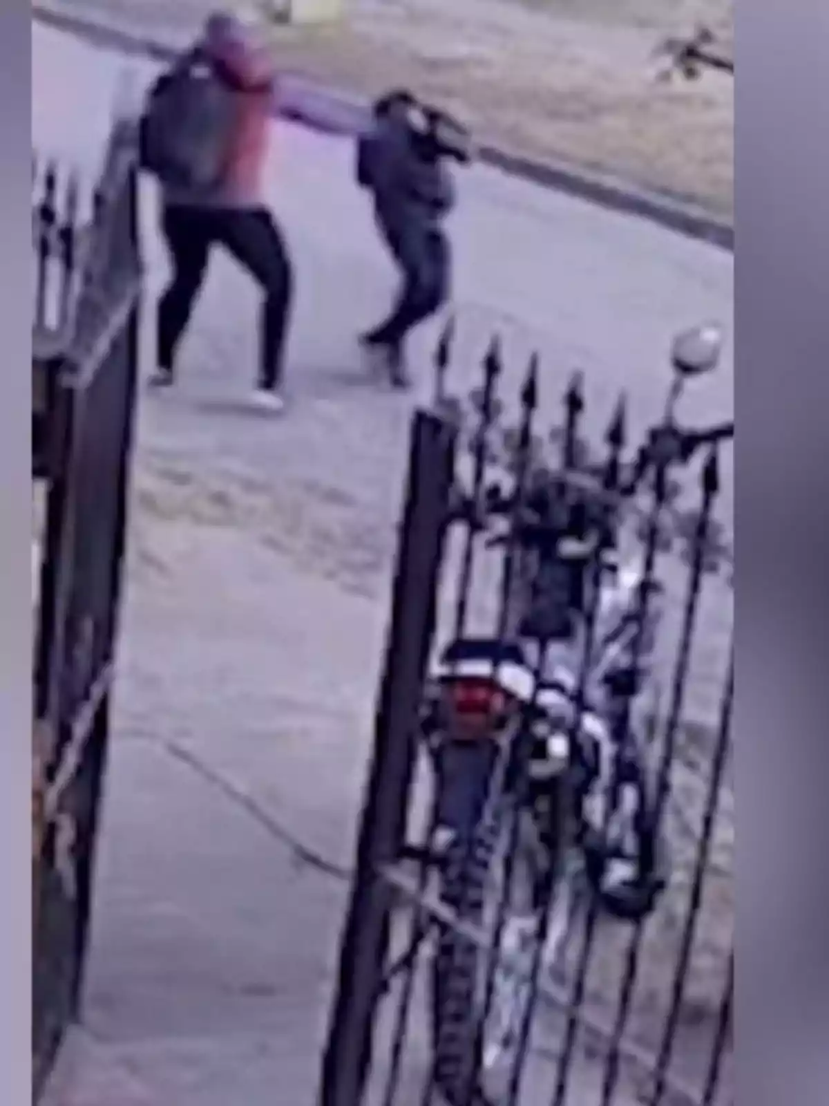 Dos personas forcejean en la calle cerca de una motocicleta estacionada junto a una reja. Dos personas forcejean en la calle cerca de una motocicleta estacionada junto a una reja.