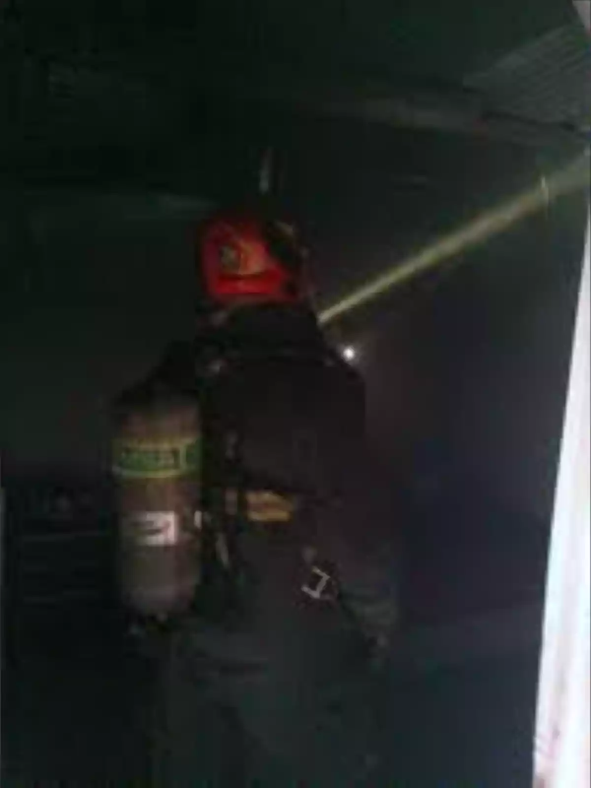 Bombero con casco rojo y equipo de respiración autónoma inspeccionando una habitación oscura con humo y usando una linterna Bombero con casco rojo y equipo de respiración autónoma inspeccionando una habitación oscura con humo y usando una linterna