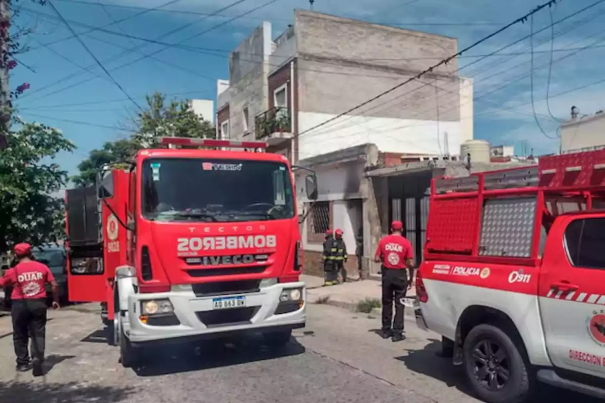 Camión de bomberos y vehículo de emergencia estacionados en una calle residencial mientras varios bomberos y rescatistas trabajan en la escena Camión de bomberos y vehículo de emergencia estacionados en una calle residencial mientras varios bomberos y rescatistas trabajan en la escena