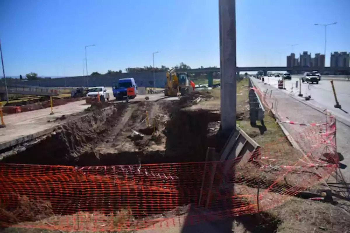 Roadworks with machinery and vehicles next to a deep trench marked by orange safety mesh on an urban avenue Roadworks with machinery and vehicles next to a deep trench marked by orange safety mesh on an urban avenue