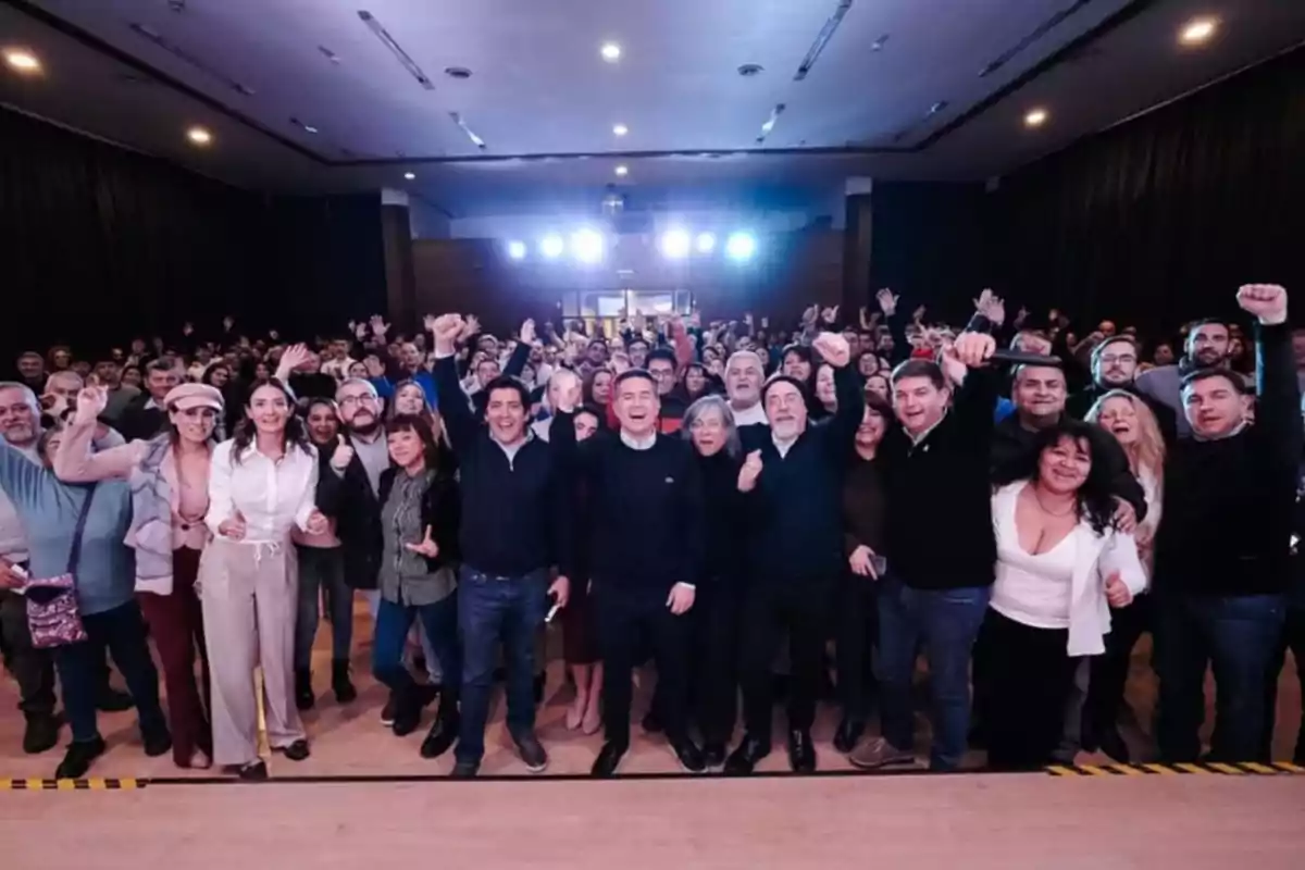 Grupo numeroso de personas reunidas en un salón, muchas de ellas sonríen y levantan los brazos en señal de celebración Grupo numeroso de personas reunidas en un salón, muchas de ellas sonríen y levantan los brazos en señal de celebración