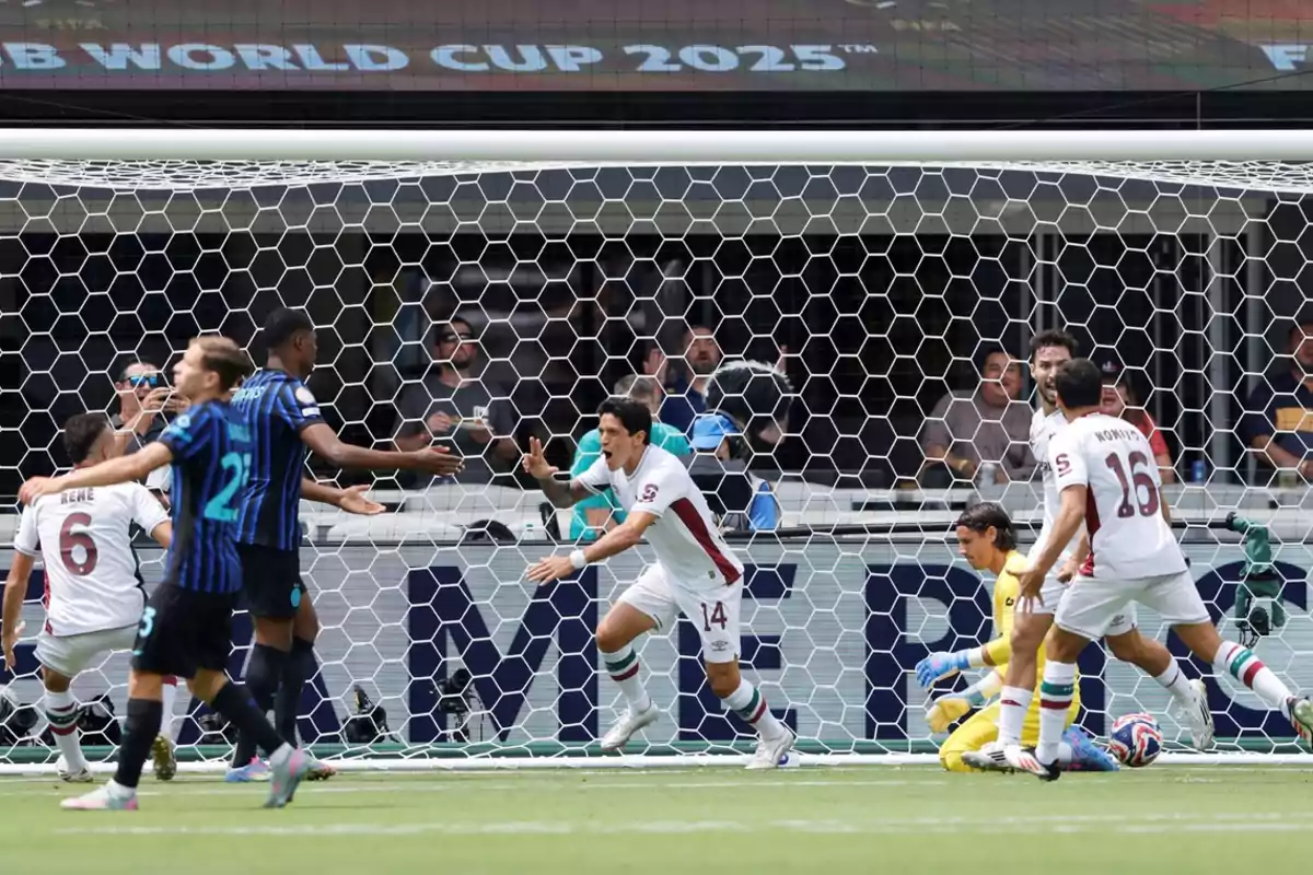 Soccer players celebrate a goal in front of the goal while the opposing goalkeeper remains on the ground and the fans watch from the stands. Soccer players celebrate a goal in front of the goal while the opposing goalkeeper remains on the ground and the fans watch from the stands.