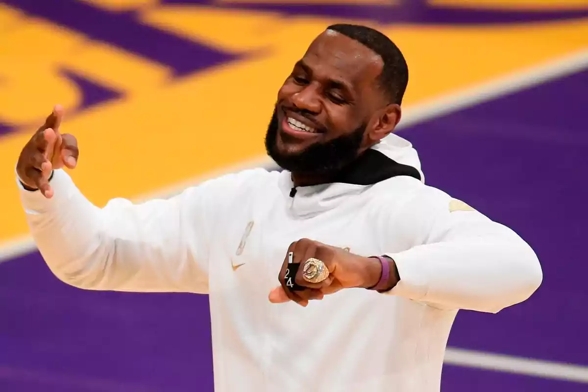 Smiling man with a beard and a white sweatjersey showing off a large ring on a basketball court Smiling man with a beard and a white sweatjersey showing off a large ring on a basketball court