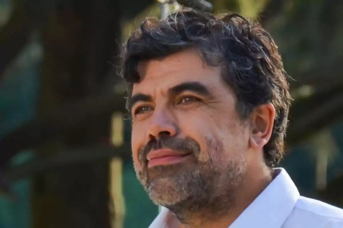 Curly-haired man with a beard wearing a white jersey looking toward the horizon in a natural setting