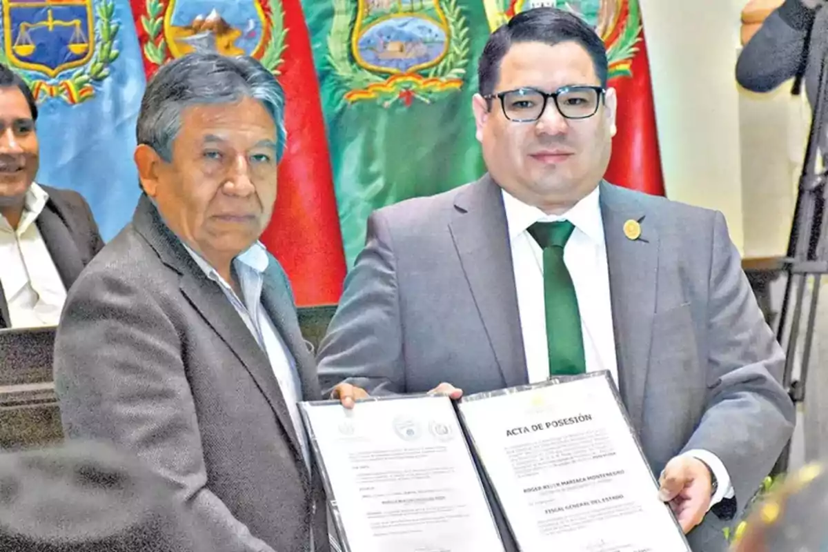 Two men in suits pose together holding a document at a formal event with flags in the background. Two men in suits pose together holding a document at a formal event with flags in the background.