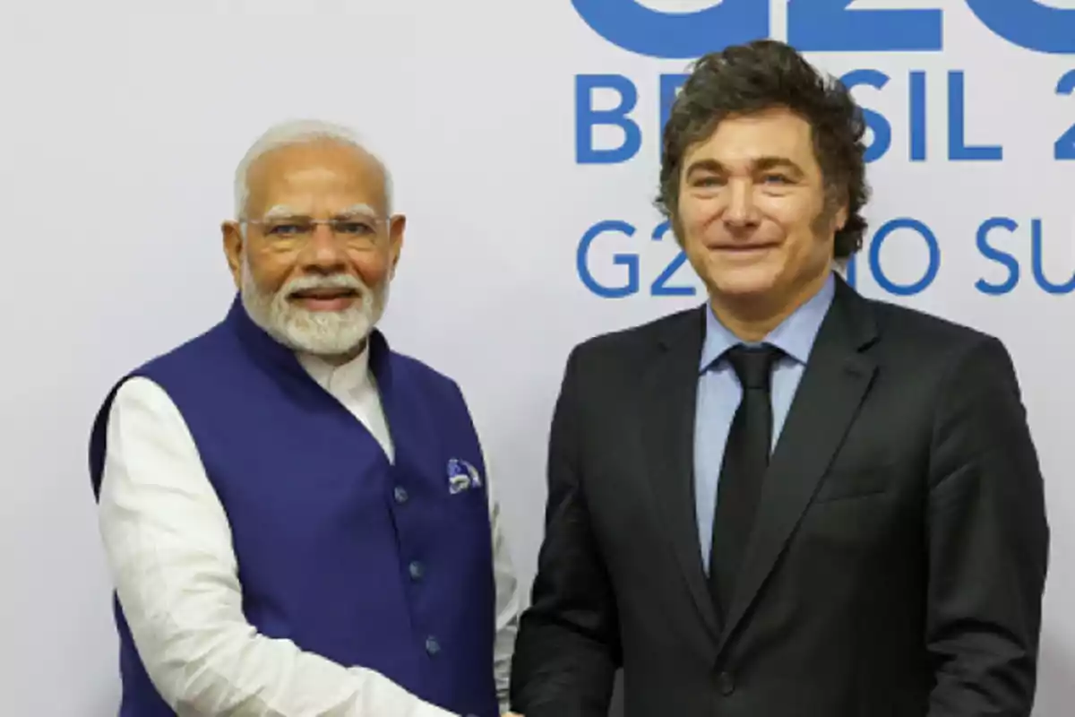 Two men in suits shake hands and smile in front of a background with blue letters referencing the G20 in Brazil.