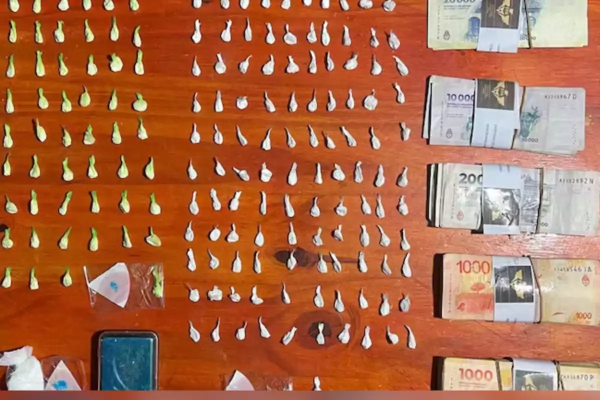 Pequeños envoltorios de droga y fajos de billetes organizados sobre una mesa de madera Pequeños envoltorios de droga y fajos de billetes organizados sobre una mesa de madera