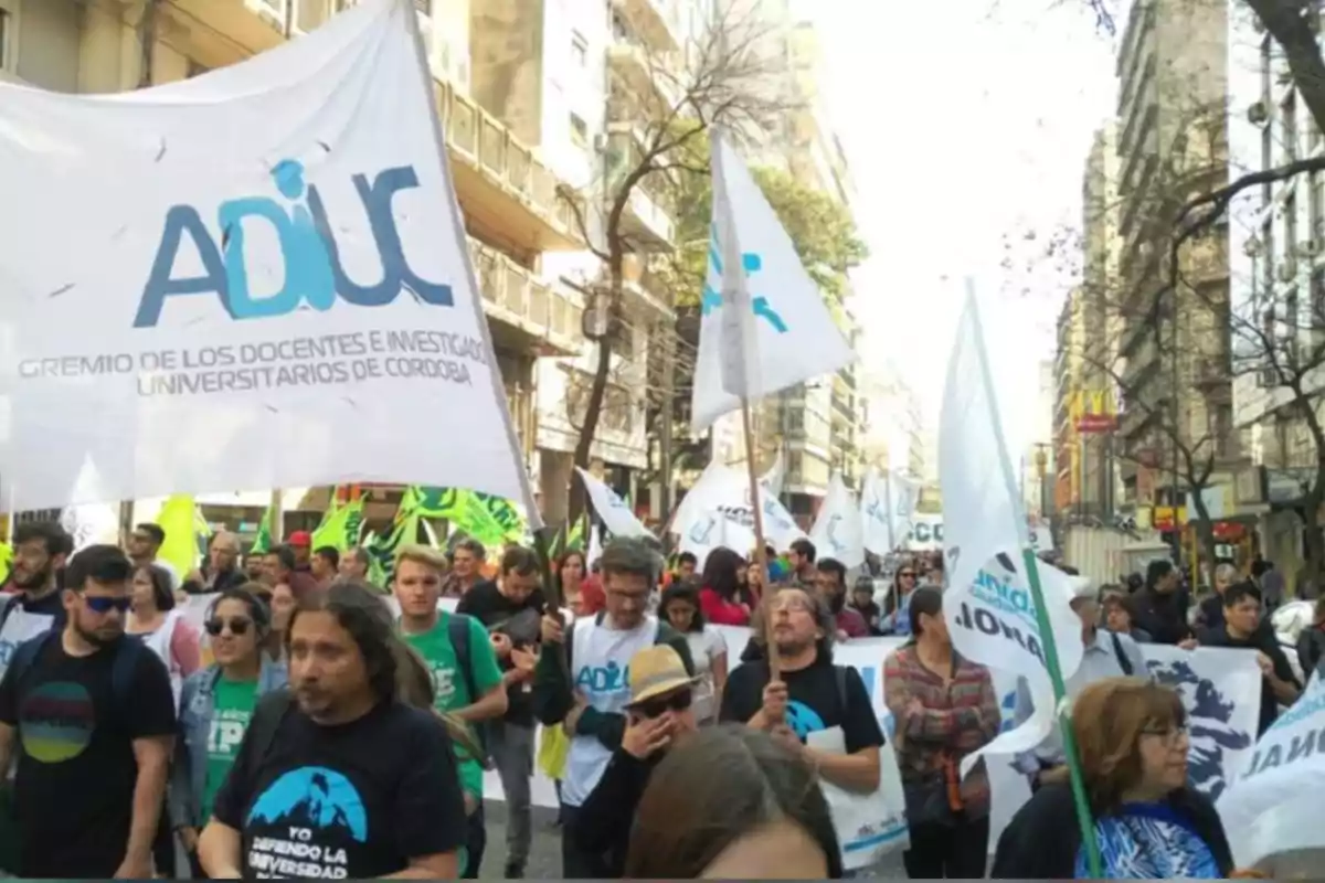 Demonstration of teachers and university students marching down a street with ADIUC flags in defense of public universities Demonstration of teachers and university students marching down a street with ADIUC flags in defense of public universities
