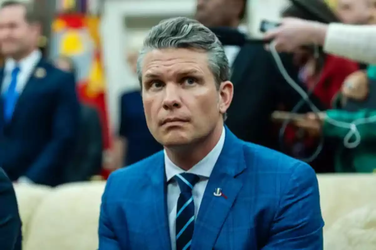 Gray-haired man in a blue suit sitting at a formal event with blurred people in the background Gray-haired man in a blue suit sitting at a formal event with blurred people in the background