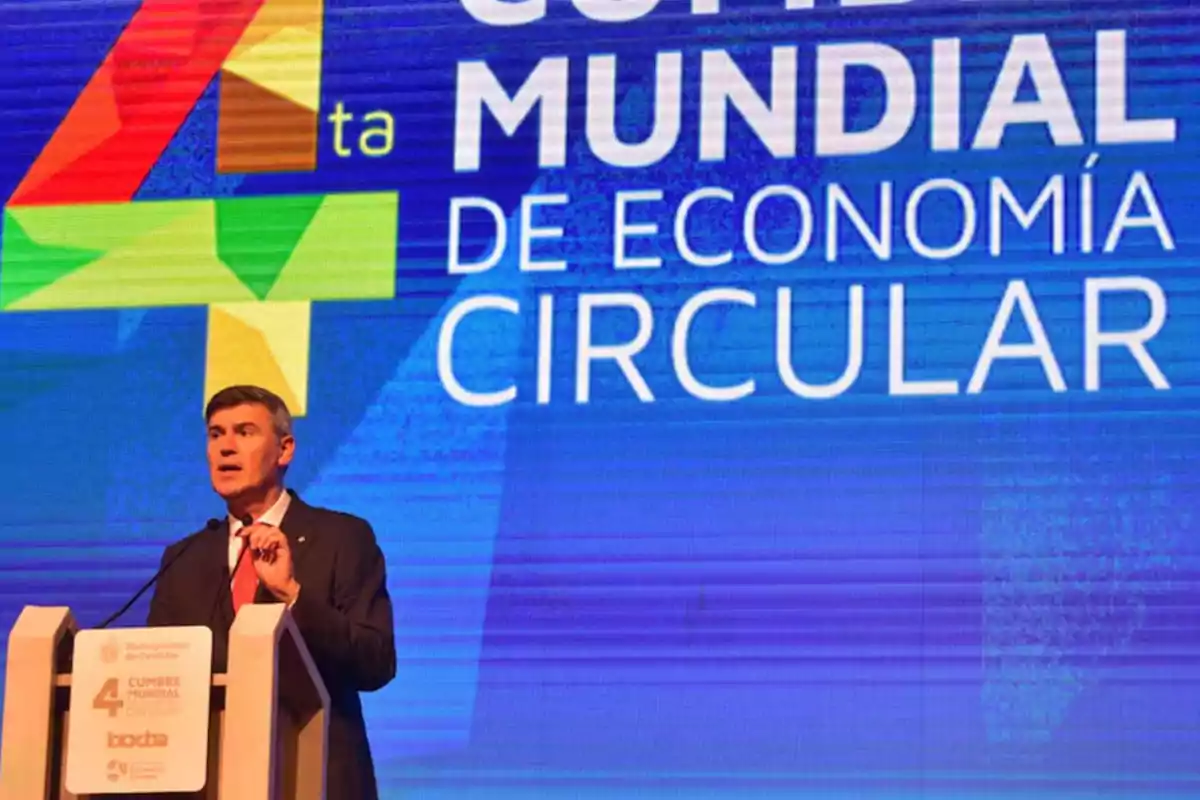 Man in a suit speaking at a podium during the Fourth World Circular Economy Forum with a blue screen in the background displaying the name of the event. Man in a suit speaking at a podium during the Fourth World Circular Economy Forum with a blue screen in the background displaying the name of the event.