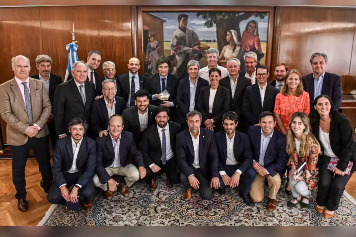Group of people posing for a formal photo in a room with wooden walls and a carpet; in the background, there is a flag and a large painting. Group of people posing for a formal photo in a room with wooden walls and a carpet; in the background, there is a flag and a large painting.
