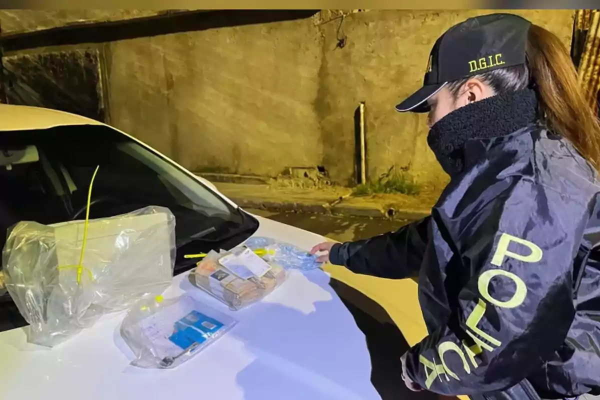 Agente de policía revisando evidencia asegurada sobre el cofre de un automóvil blanco durante un operativo nocturno