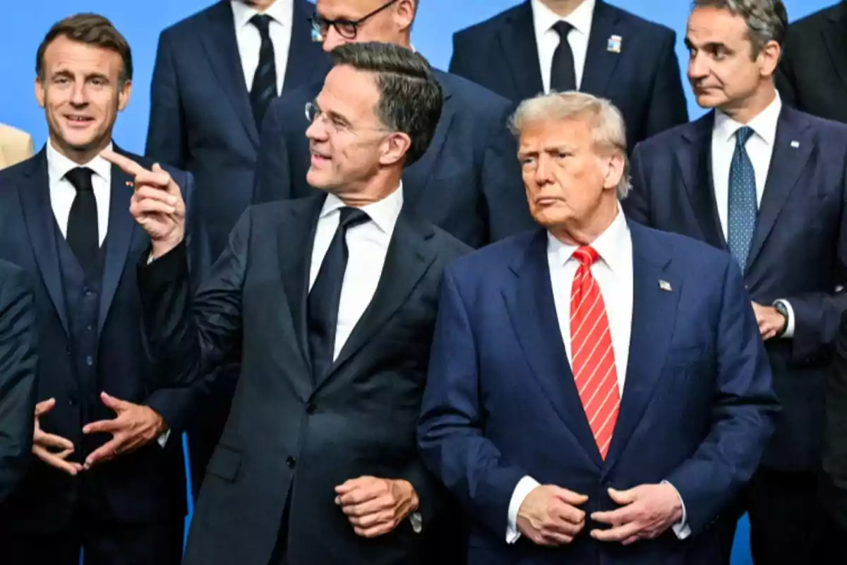 Several men in dark suits pose together at a formal event against a blue background. Several men in dark suits pose together at a formal event against a blue background.