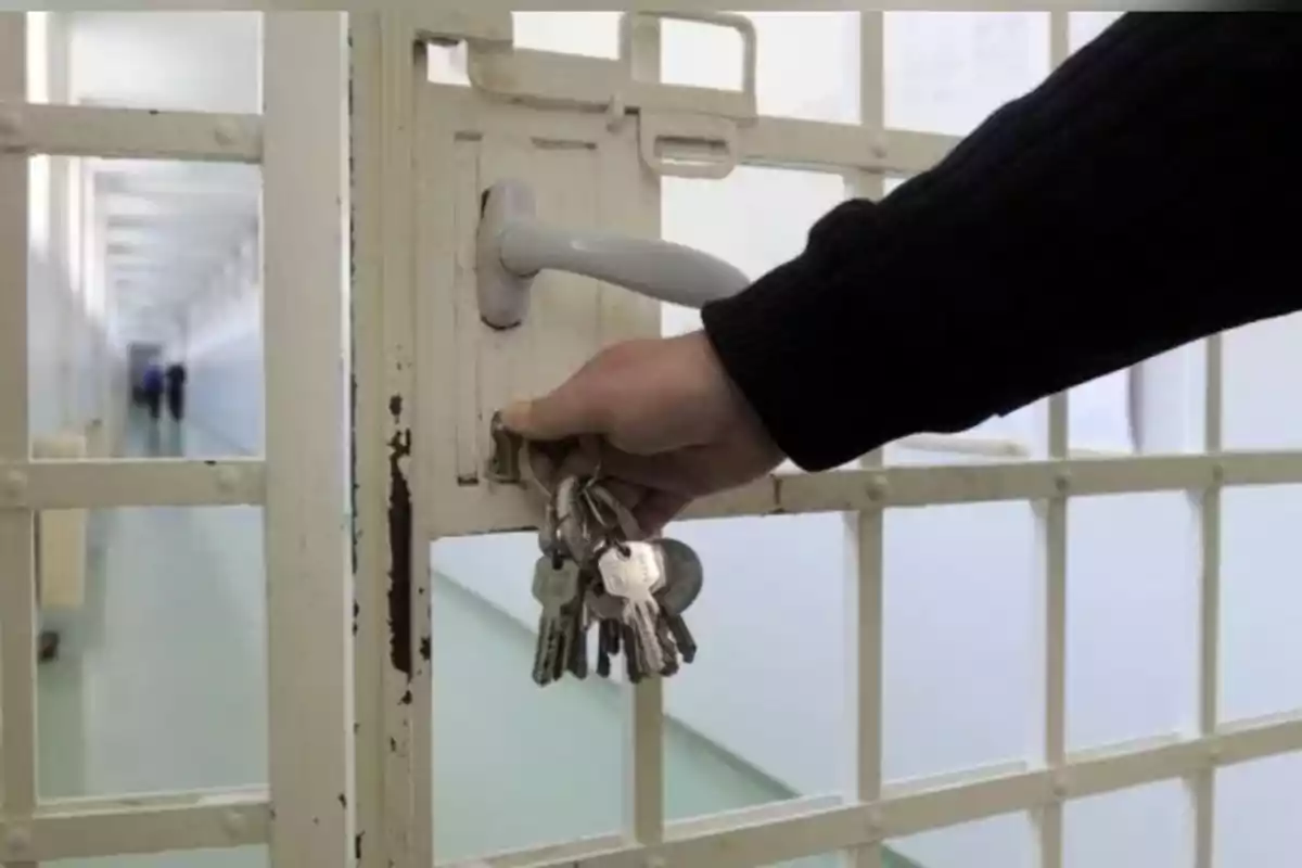 Persona abriendo una puerta de celda con un manojo de llaves en una prisión