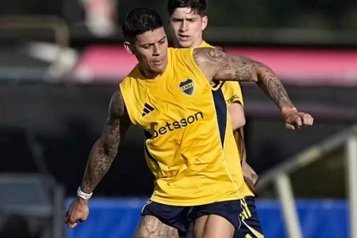 Dos futbolistas entrenan con el uniforme amarillo de Boca Juniors en una cancha al aire libre Dos futbolistas entrenan con el uniforme amarillo de Boca Juniors en una cancha al aire libre
