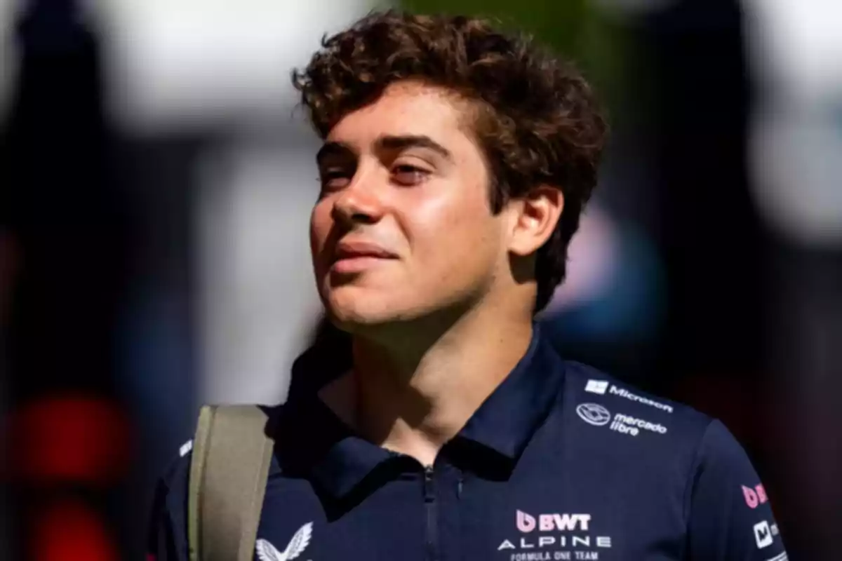 Joven con cabello rizado y camiseta azul marino con logos de patrocinadores mirando hacia un lado bajo la luz del sol