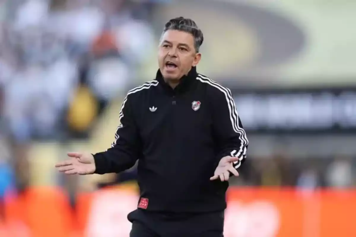 Soccer coach wearing a black River Plate jacket gesturing on the field during a match