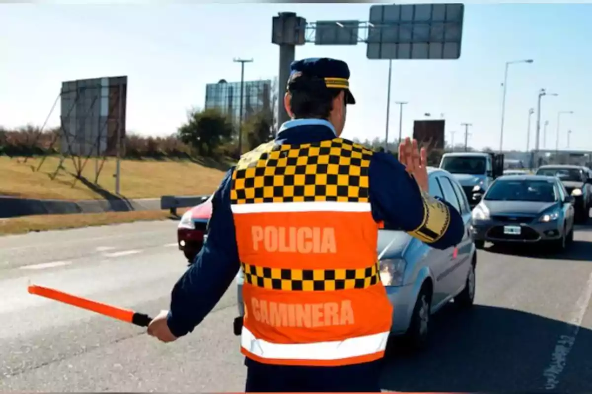 Agente de policía vial deteniendo el tráfico en una carretera mientras sostiene una vara luminosa y lleva un chaleco reflectante naranja Agente de policía vial deteniendo el tráfico en una carretera mientras sostiene una vara luminosa y lleva un chaleco reflectante naranja