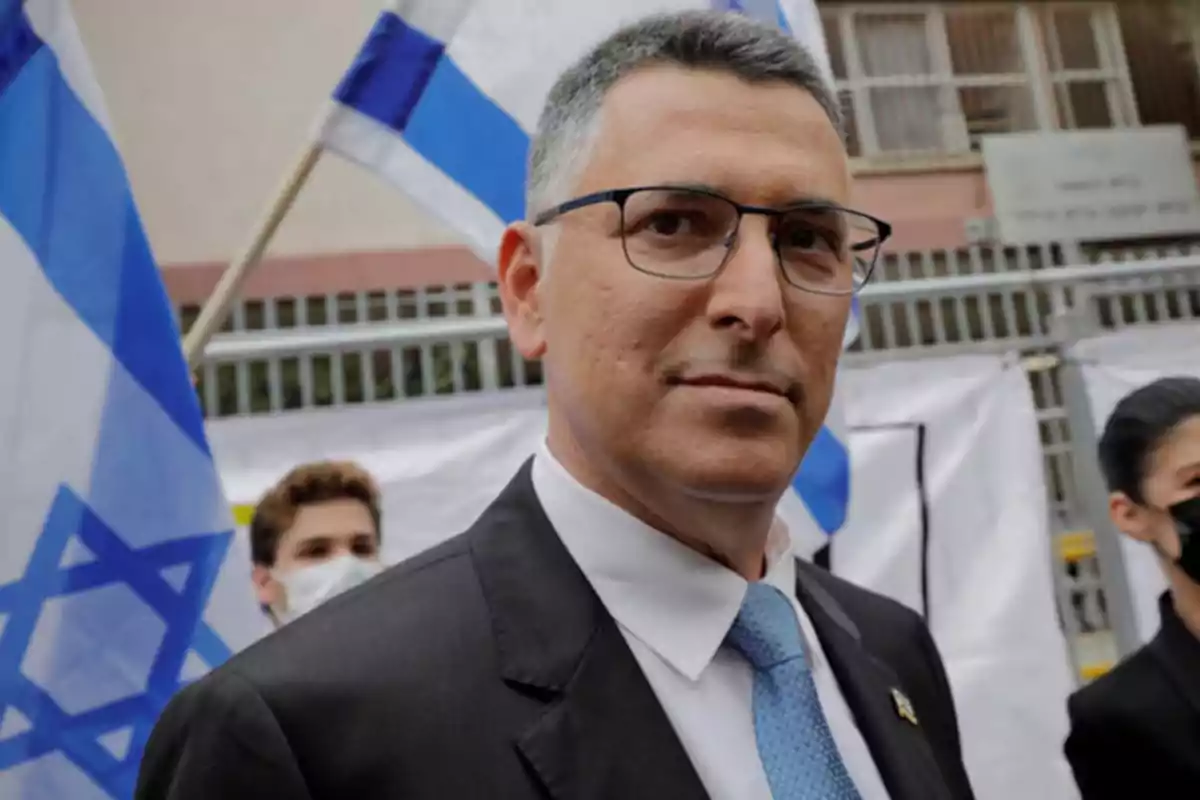 Man with glasses and a suit posing in front of Israeli flags at an outdoor event Man with glasses and a suit posing in front of Israeli flags at an outdoor event