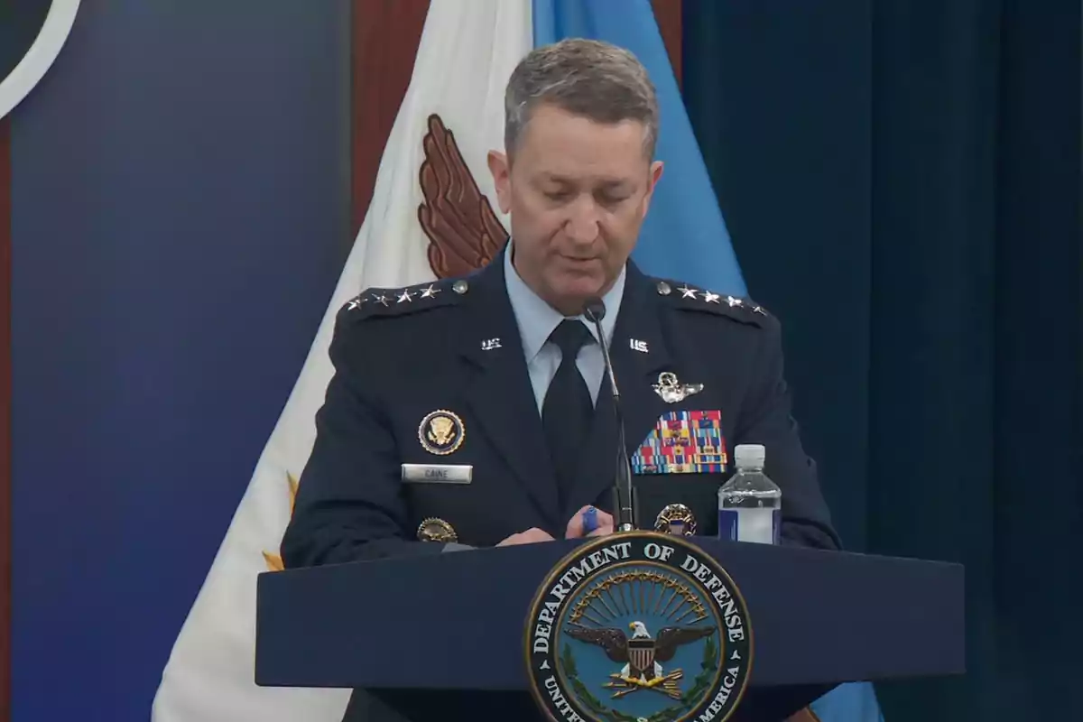 A United States Air Force general speaks at a Department of Defense podium with flags in the background and a bottle of water at his side. A United States Air Force general speaks at a Department of Defense podium with flags in the background and a bottle of water at his side.