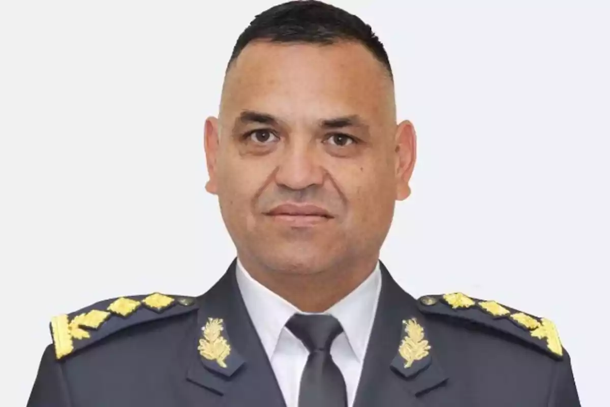 Hombre con uniforme militar oscuro y detalles dorados mirando al frente sobre fondo claro Hombre con uniforme militar oscuro y detalles dorados mirando al frente sobre fondo claro