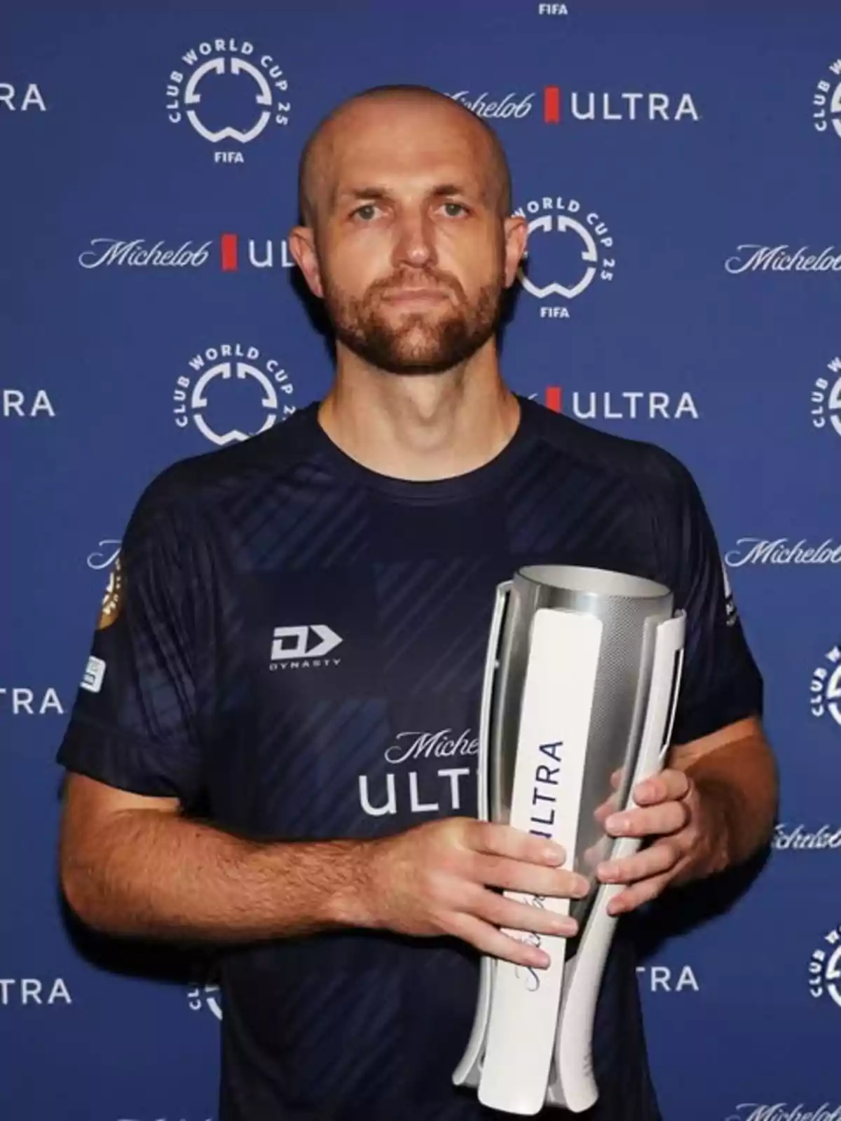 Man in a dark blue sports jersey holding a silver trophy in front of a blue background with Club World Cup and Michelob Ultra logos Man in a dark blue sports jersey holding a silver trophy in front of a blue background with Club World Cup and Michelob Ultra logos