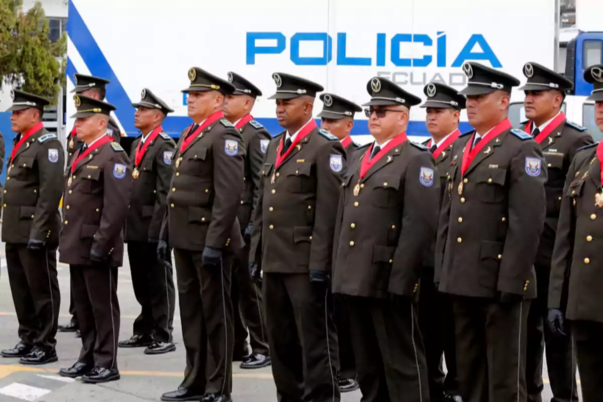 Grupo de policías uniformados de pie en formación durante una ceremonia frente a un vehículo oficial