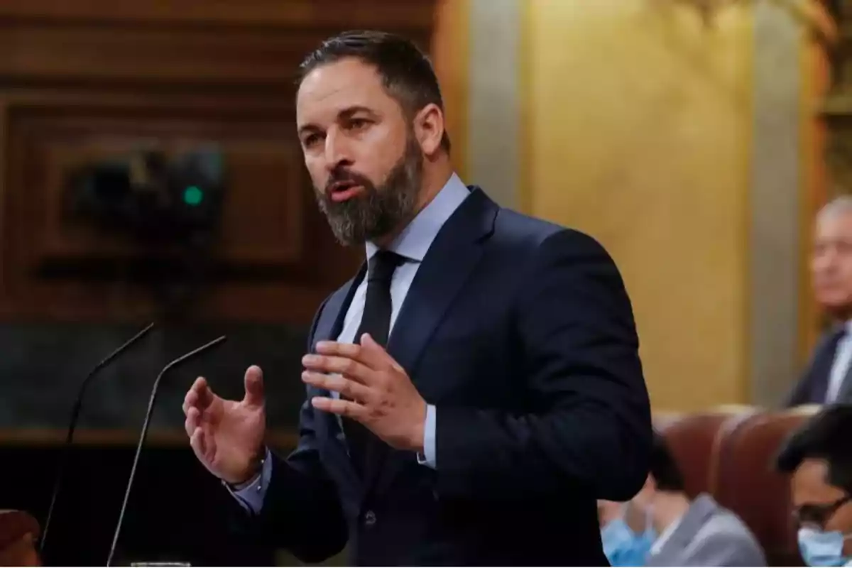 Hombre con barba y traje oscuro hablando en un podio dentro de un recinto parlamentario Hombre con barba y traje oscuro hablando en un podio dentro de un recinto parlamentario