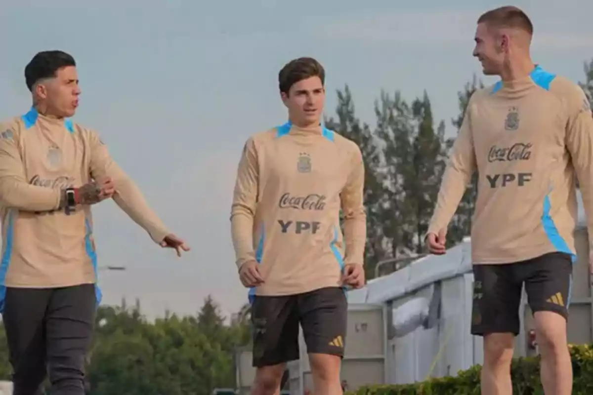 Three players in beige training uniforms walk and talk outdoors. Three players in beige training uniforms walk and talk outdoors.