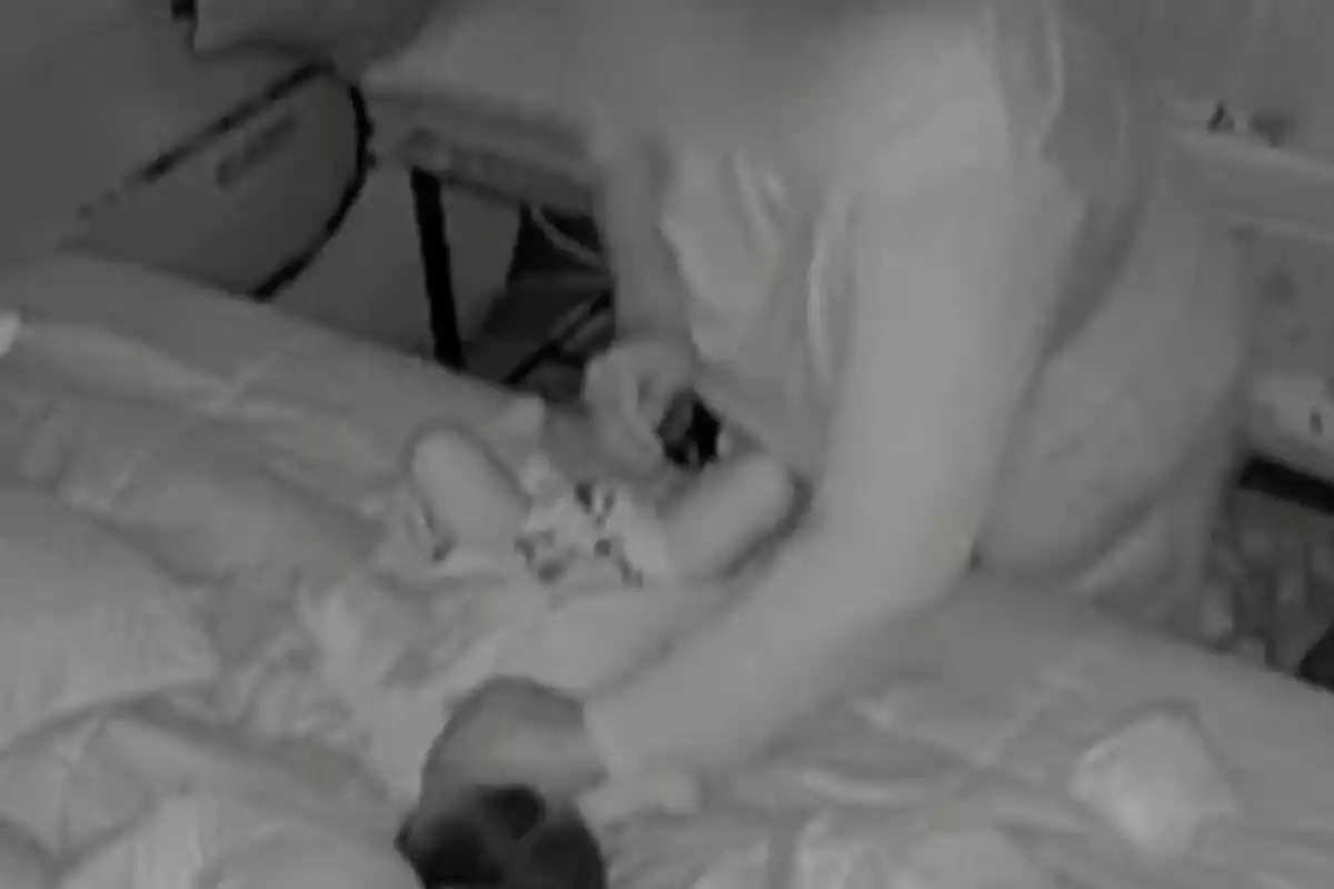 Persona inclinada sobre una cama atendiendo a un bebé acostado en un ambiente interior con poca luz
