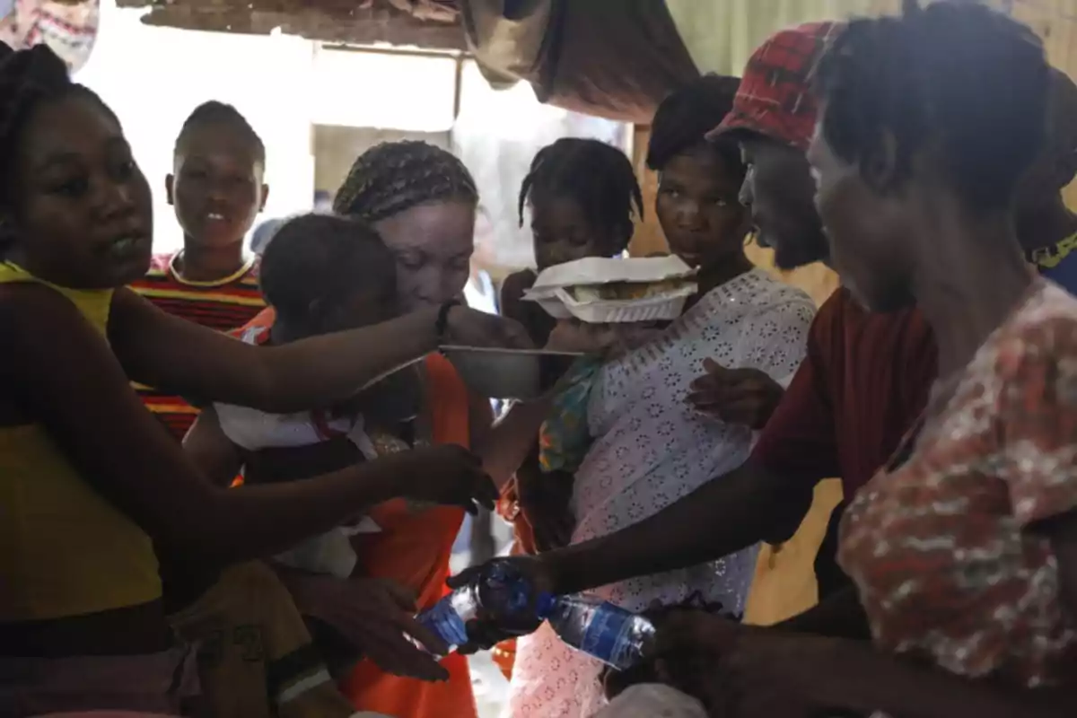 Varias personas se reúnen en un espacio cerrado mientras reparten comida y botellas de agua Varias personas se reúnen en un espacio cerrado mientras reparten comida y botellas de agua