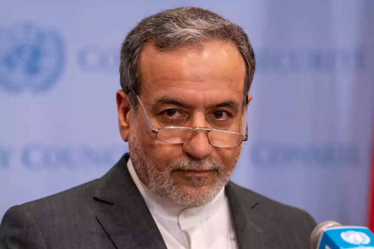 Middle-aged man with a beard and glasses, dressed in a formal suit, speaking in front of a blue microphone with the UN logo blurred in the background Middle-aged man with a beard and glasses, dressed in a formal suit, speaking in front of a blue microphone with the UN logo blurred in the background