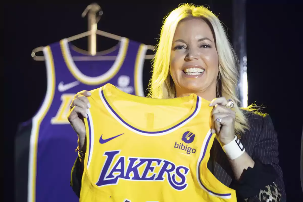 Smiling woman holds a yellow Lakers jersey with another purple jersey hanging in the background Smiling woman holds a yellow Lakers jersey with another purple jersey hanging in the background