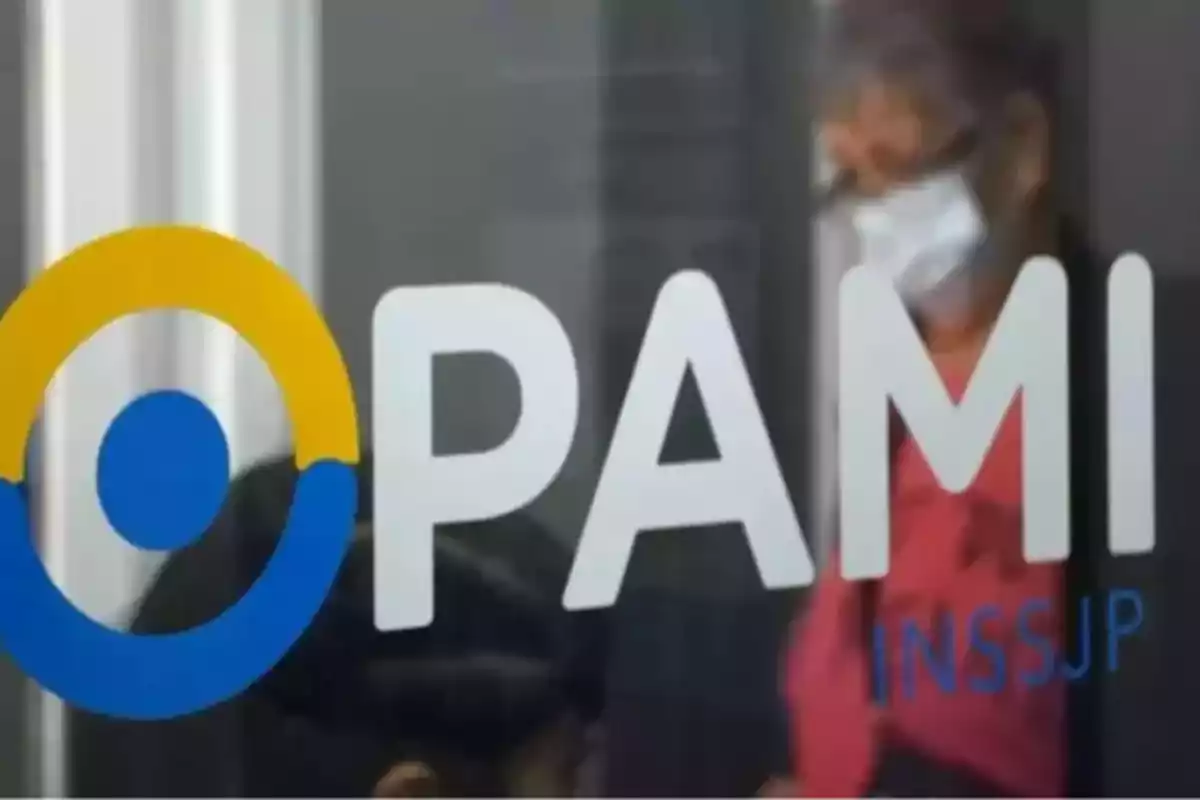 Logo de PAMI en una puerta de vidrio con una persona mayor usando barbijo al fondo Logo de PAMI en una puerta de vidrio con una persona mayor usando barbijo al fondo