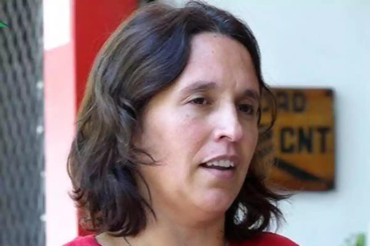 Mujer de cabello castaño y ondulado con camiseta roja hablando en un entorno urbano Mujer de cabello castaño y ondulado con camiseta roja hablando en un entorno urbano