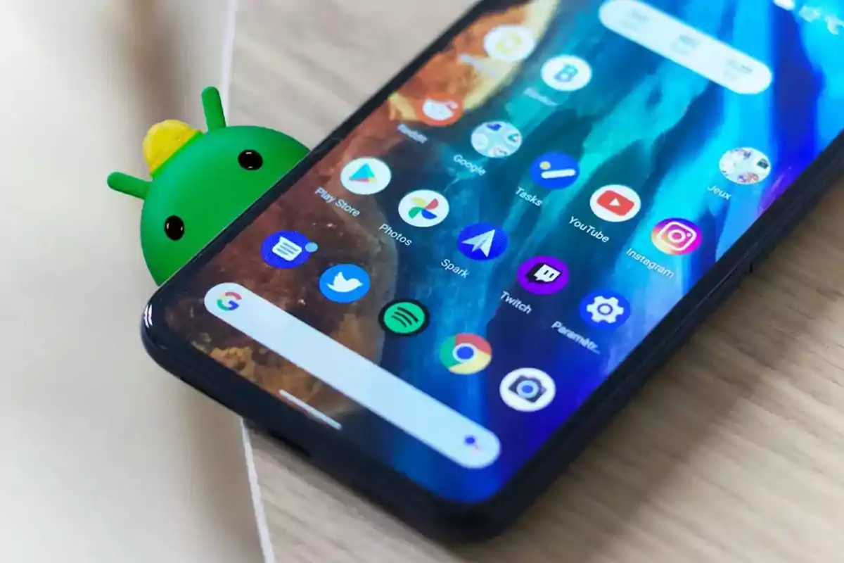 Un teléfono móvil con la pantalla encendida mostrando varias aplicaciones y una figura del androide de Android asomándose por detrás. Un teléfono móvil con la pantalla encendida mostrando varias aplicaciones y una figura del androide de Android asomándose por detrás.