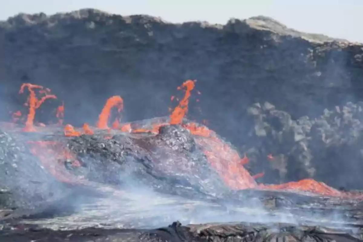 Lava incandescente brotando de un volcán activo con humo y rocas oscuras alrededor